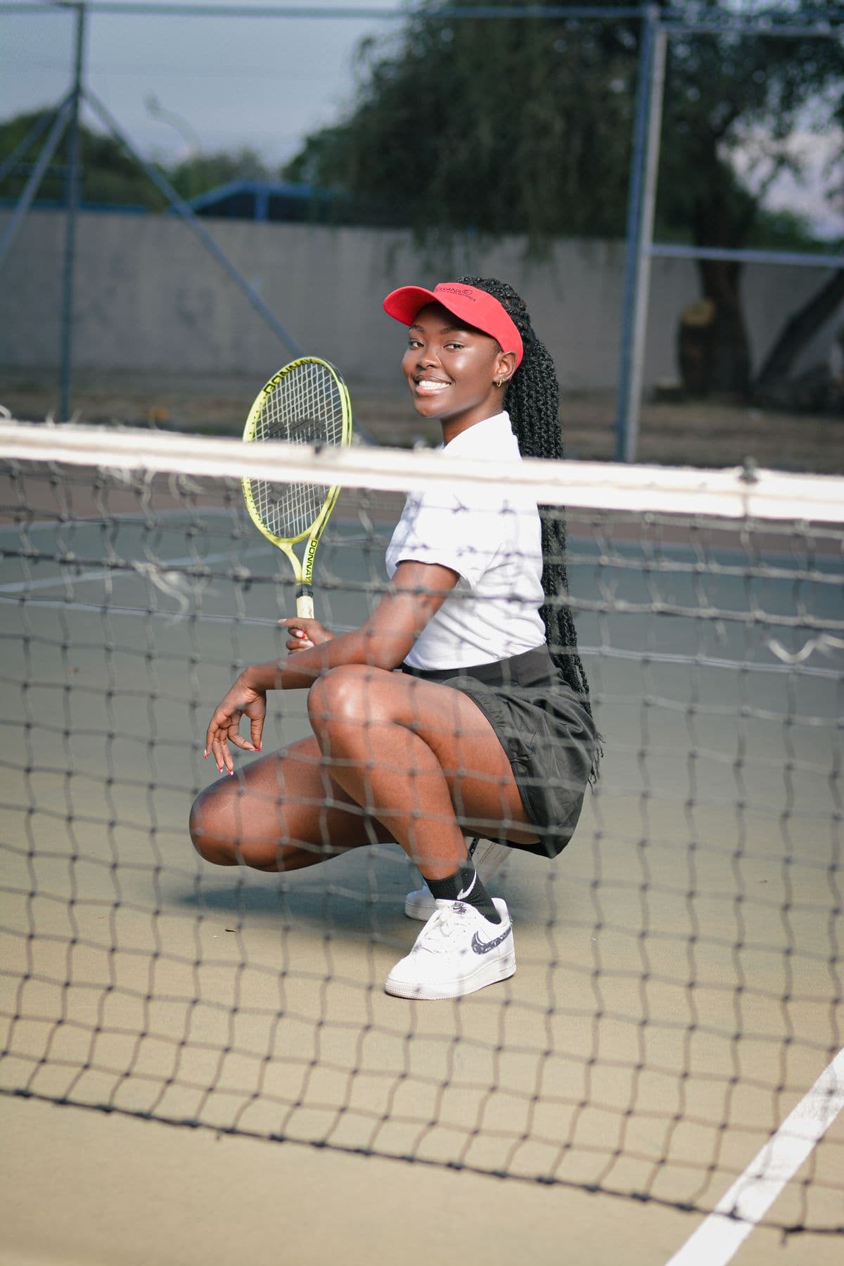 A smiling player crouching by the net with her racket